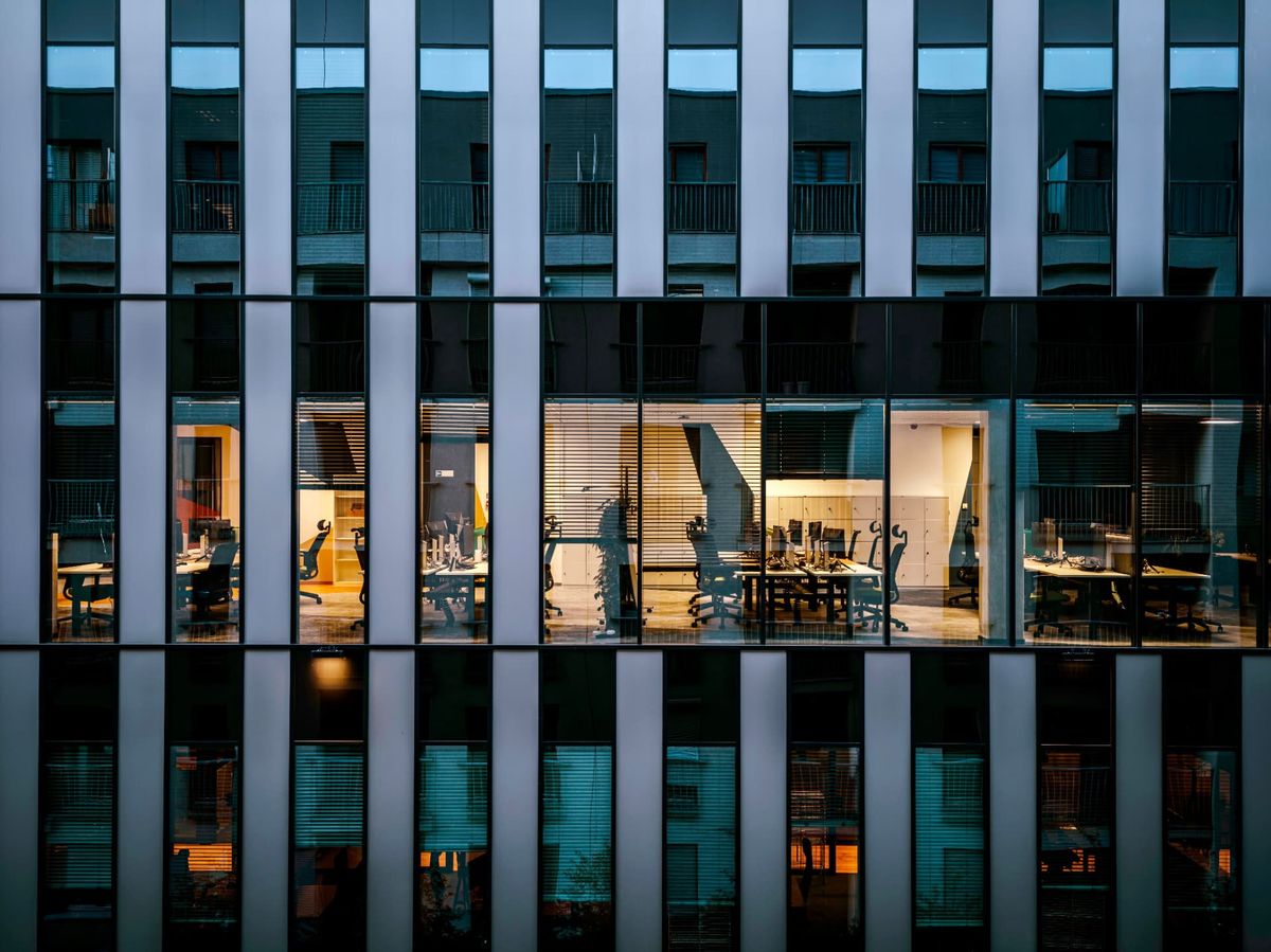 Office building at dusk with lit workspaces visible through glass windows